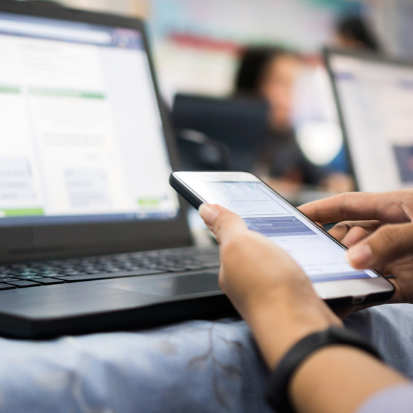 En person som sitter framför en bärbar dator och håller i en mobiltelefon.