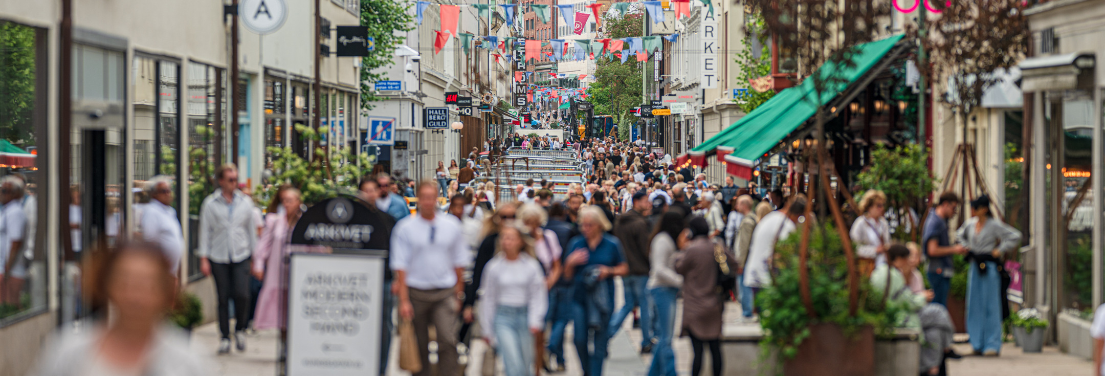 En folkmassa som går längs en gata bredvid höga byggnader.
