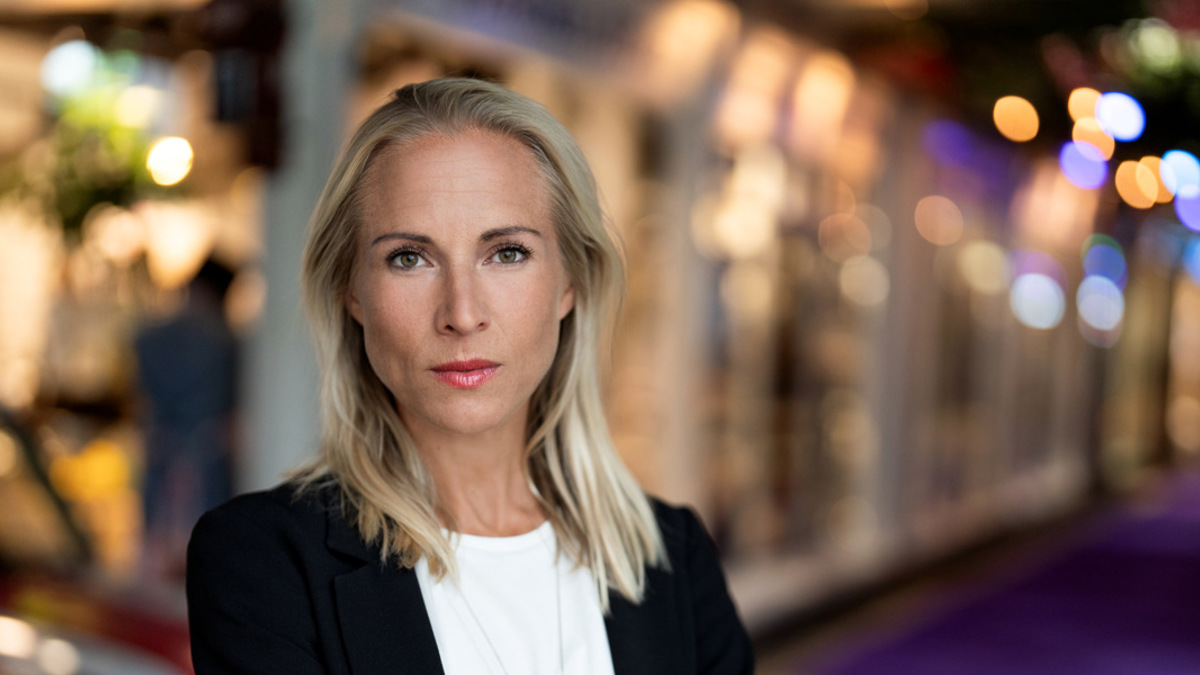 En kvinna med armarna i kors som står framför en bil.