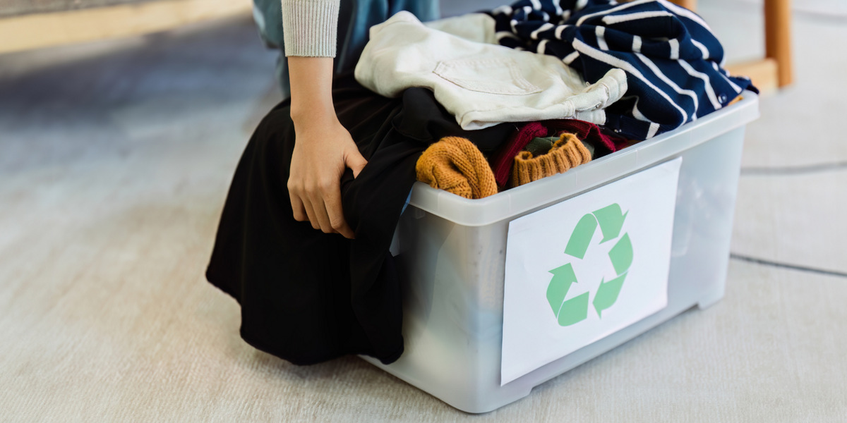 En kvinna sitter på golvet bredvid en låda fylld med kläder.