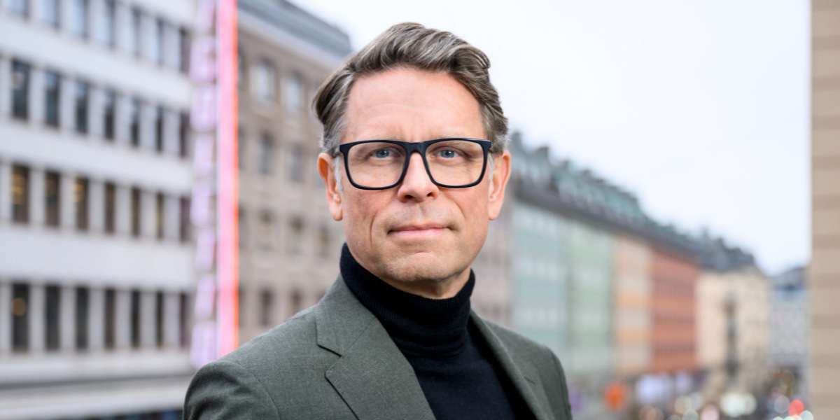 En man med glasögon som står framför en hög byggnad.