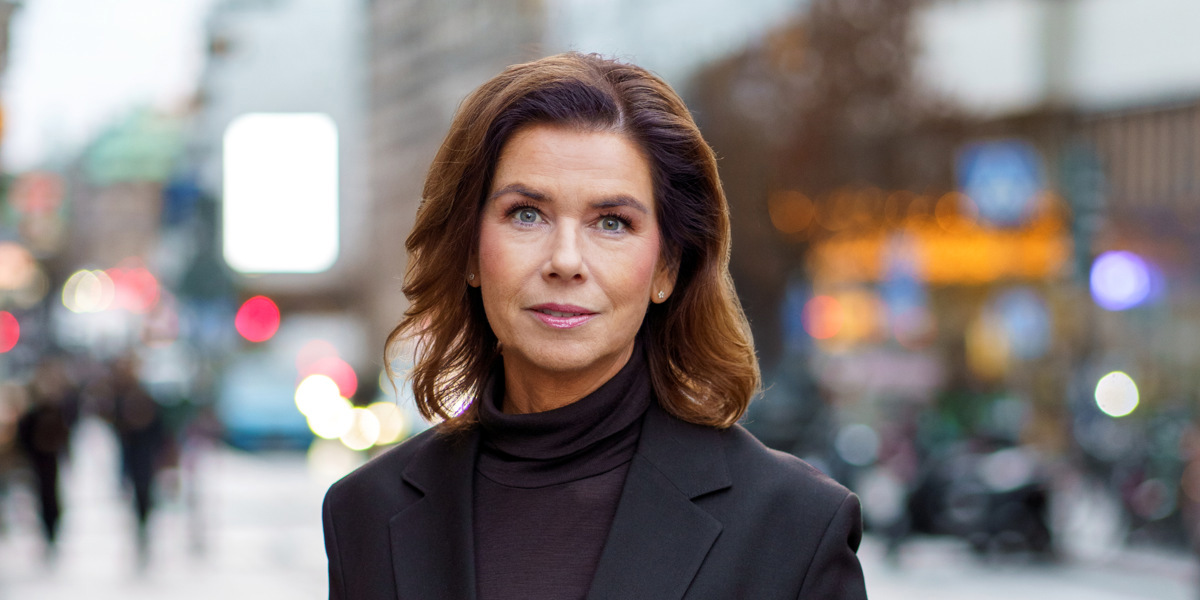 En kvinna i svart kostym står på en trottoar.