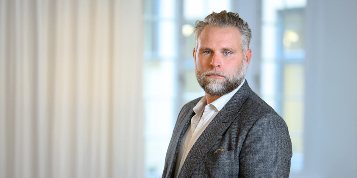 En man i kostym står framför ett fönster.