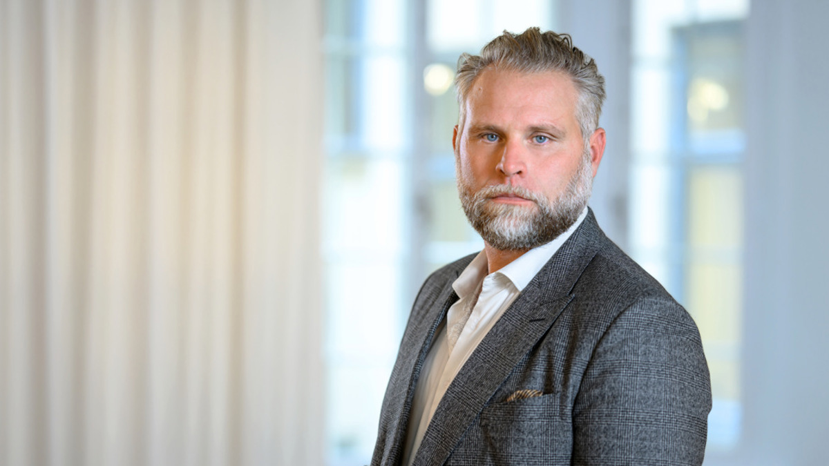 En man i kostym står framför ett fönster.