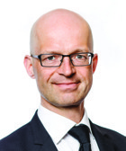 En man i kostym och slips som poserar för ett foto.