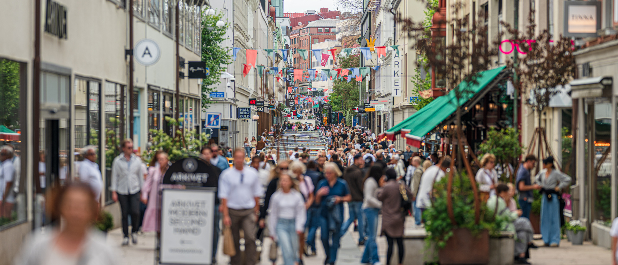En folkmassa som går längs en gata bredvid höga byggnader.