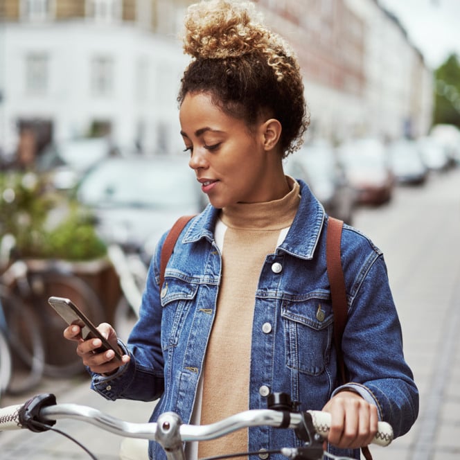 En kvinna som står bredvid en cykel och tittar på sin mobiltelefon.