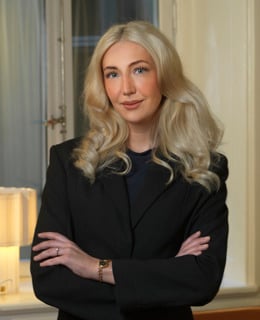 En kvinna som står framför ett fönster med armarna i kors.