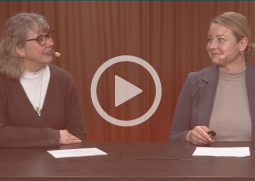 Två kvinnor sitter vid ett bord och pratar med varandra.