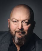 En man med skägg som sitter i en stol.