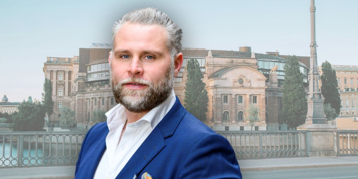 En man i blå kostym står framför en byggnad.