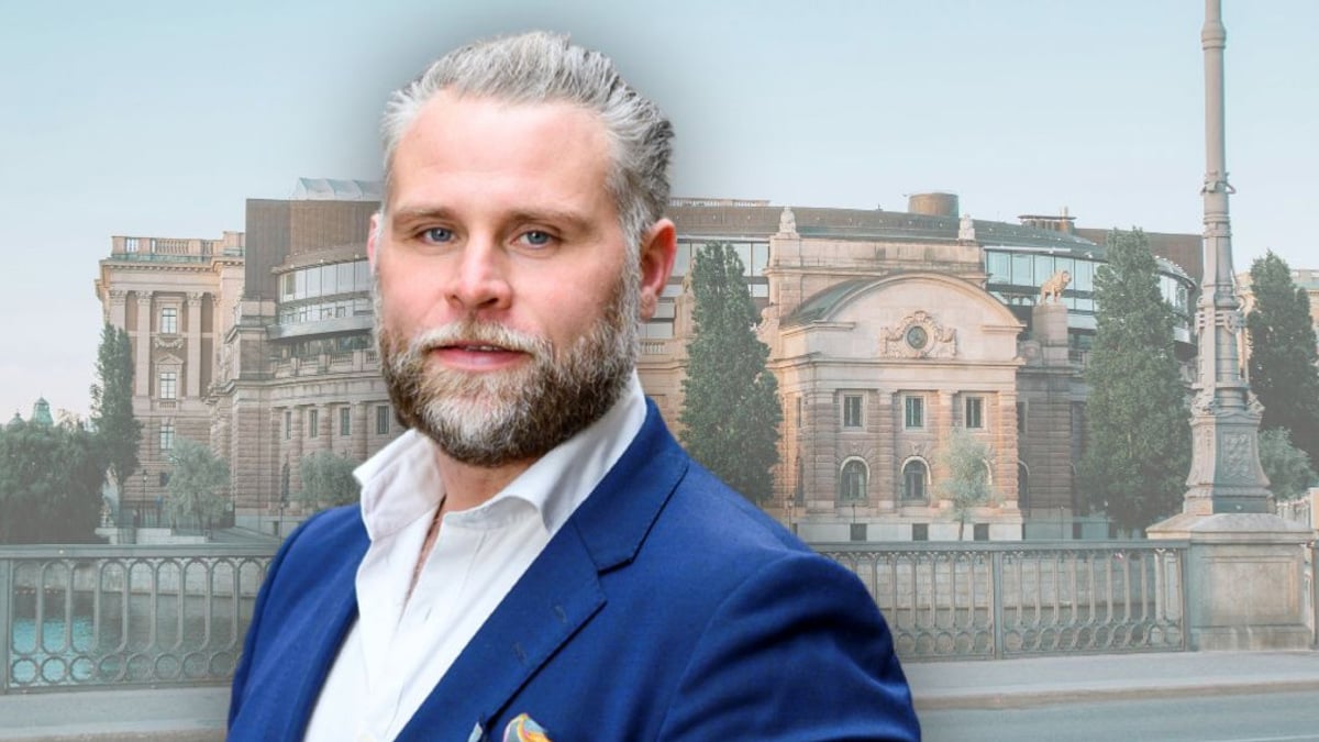 En man i blå kostym står framför en byggnad.