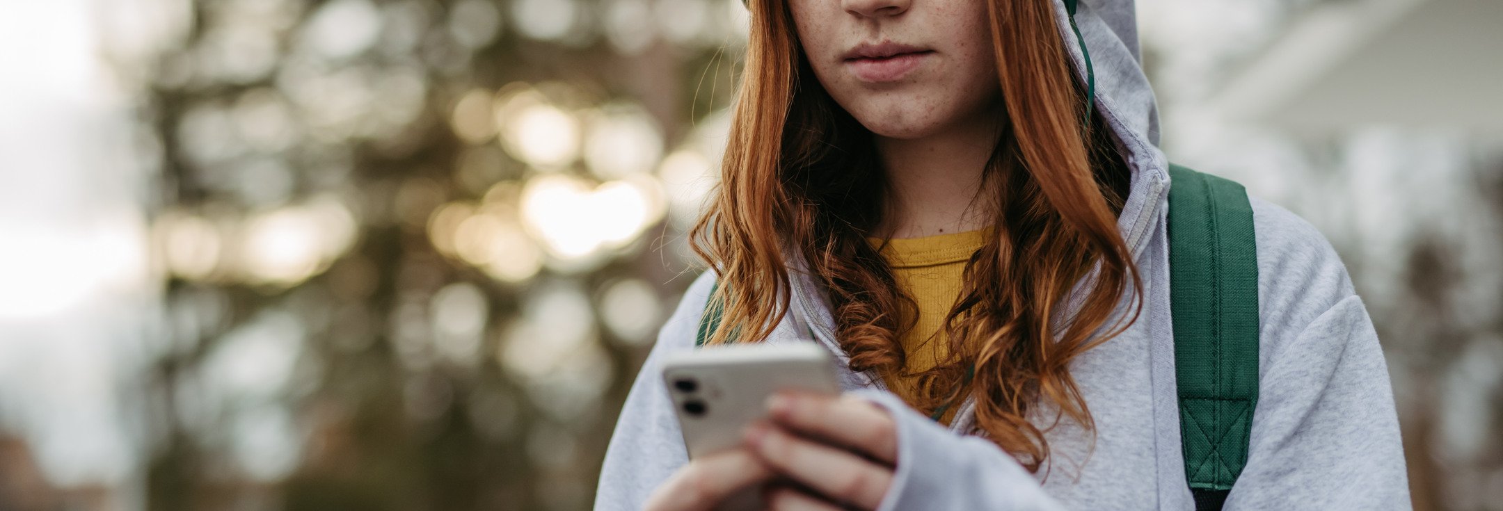 En flicka med hörlurar tittar på sin mobiltelefon.