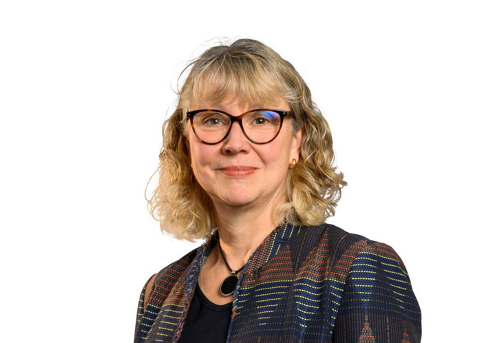 En kvinna med glasögon står framför en vit bakgrund.